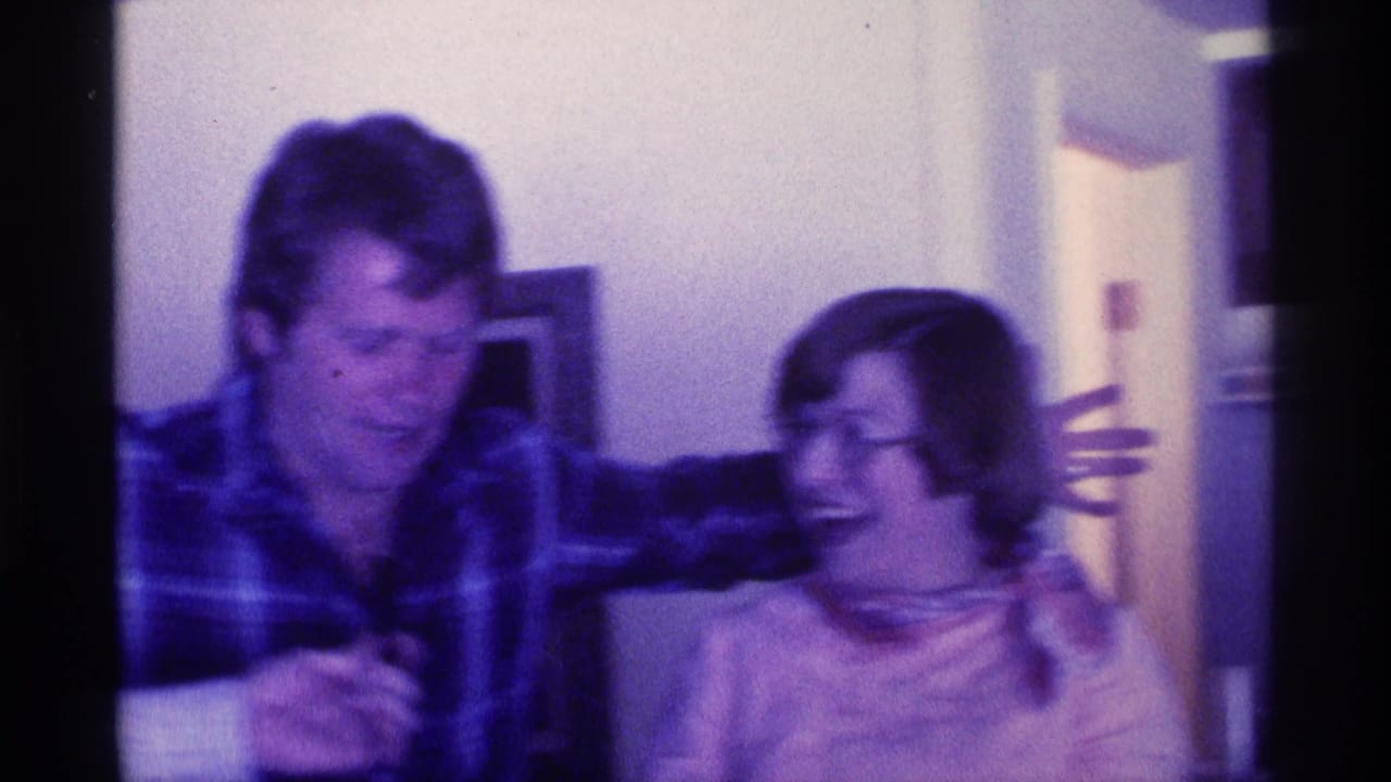 Man in plaid shirt holds a microphone beside a laughing woman in glasses.