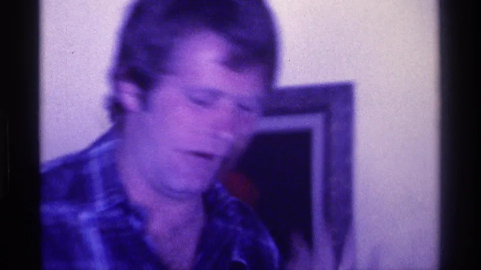 Soft-focus 1976 Kentucky 8mm close frame of a man in a plaid shirt inside a private or community interior.