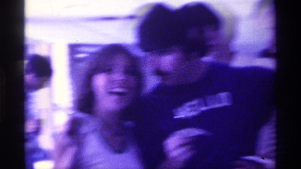 Woman smiling beside a man in a dark HELLO t-shirt during an indoor gathering.