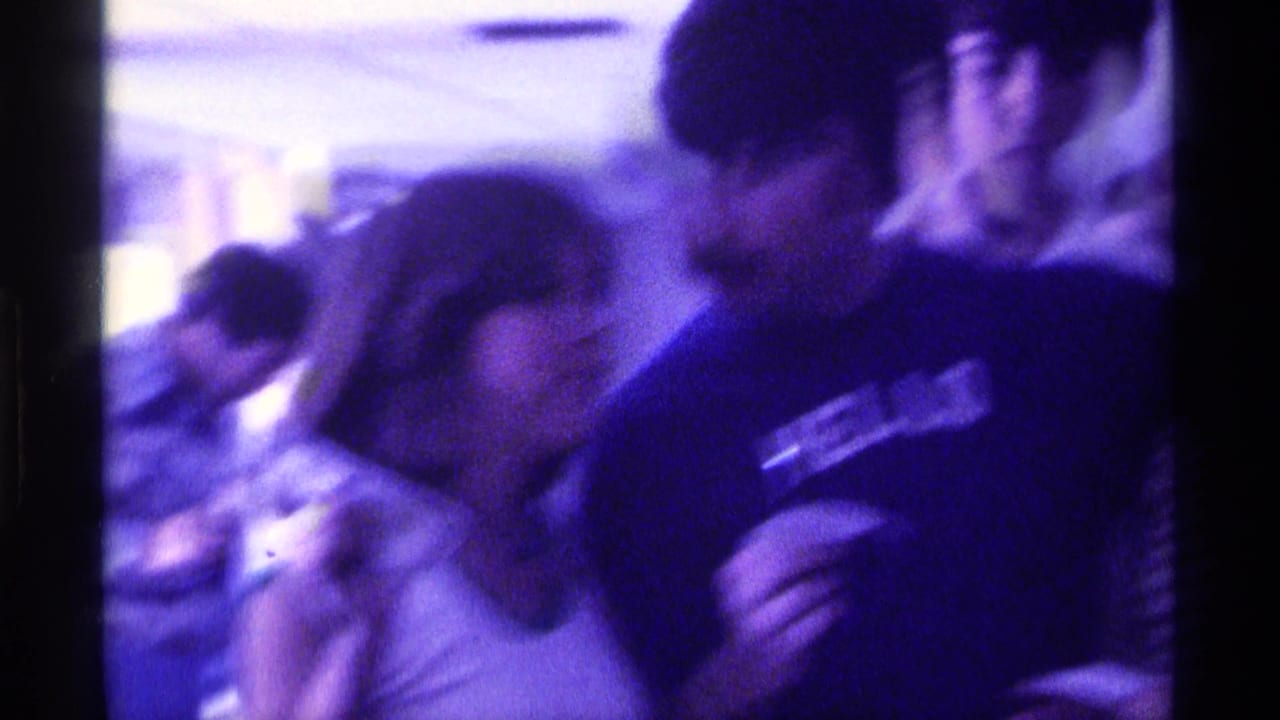 The man in the HELLO t-shirt leans near a woman while another adult man appears at the edge of the indoor Kentucky scene.