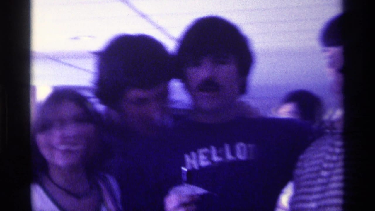 Several young adults crowd close to the camera, including one wearing a dark HELLO sweatshirt.
