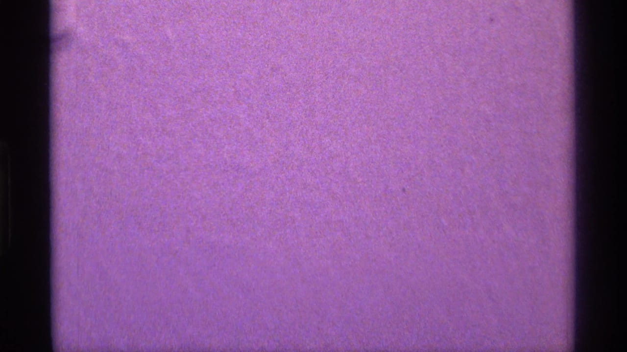 A purple, softly exposed 8mm frame with little visible subject detail and a dark film-edge border along the left side.