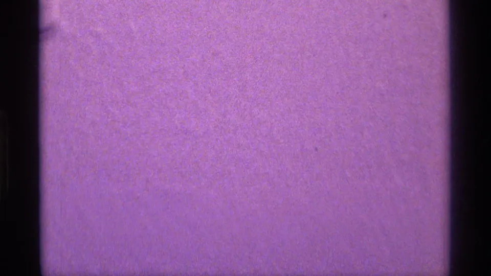 A purple, softly exposed 8mm frame with little visible subject detail and a dark film-edge border along the left side.