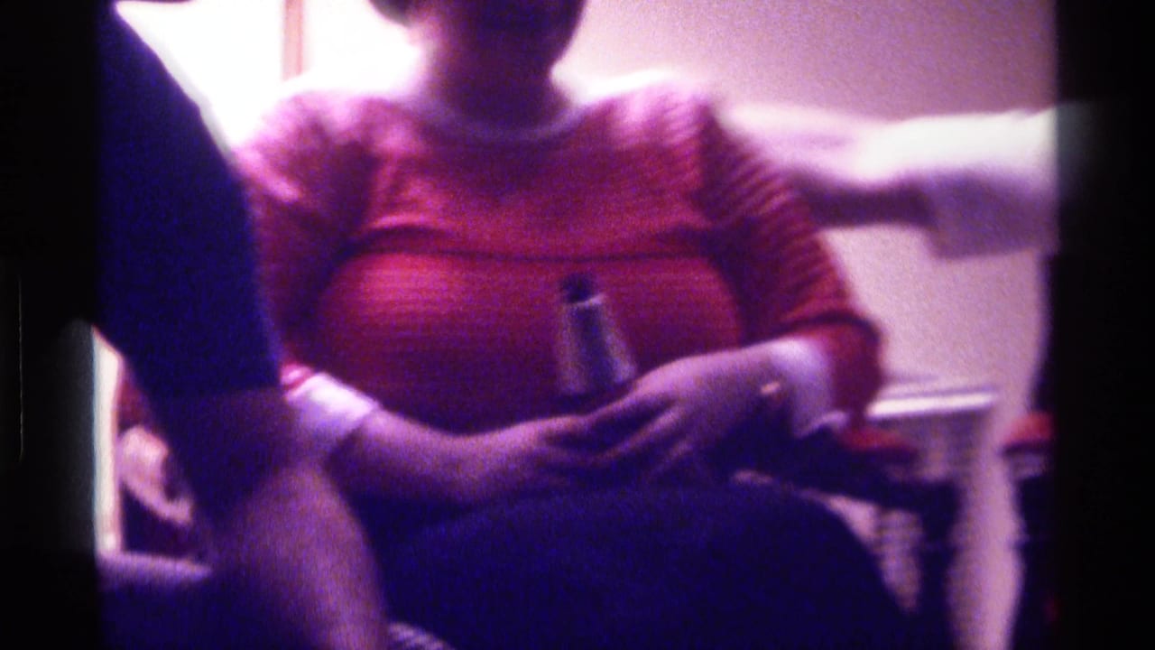 Seated woman in a striped red sweater holds a bottle in a dim room.