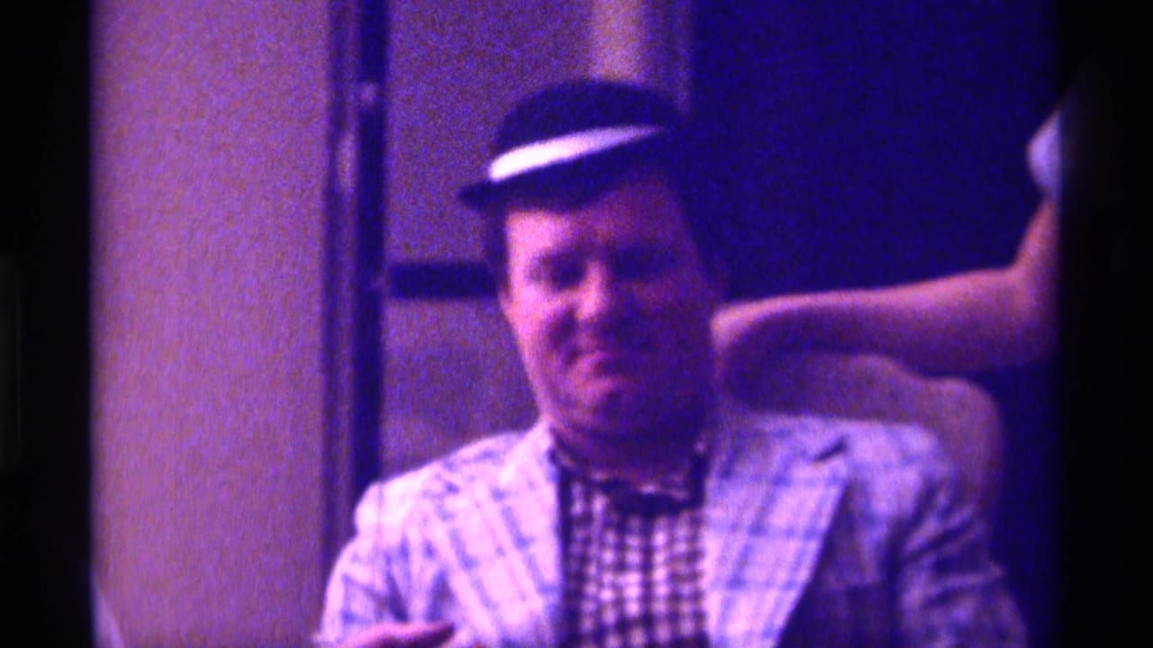 The seated man in a dark hat and plaid jacket remains framed in a purple-shifted 1976 Kentucky interior, with a partial arm visible nearby.