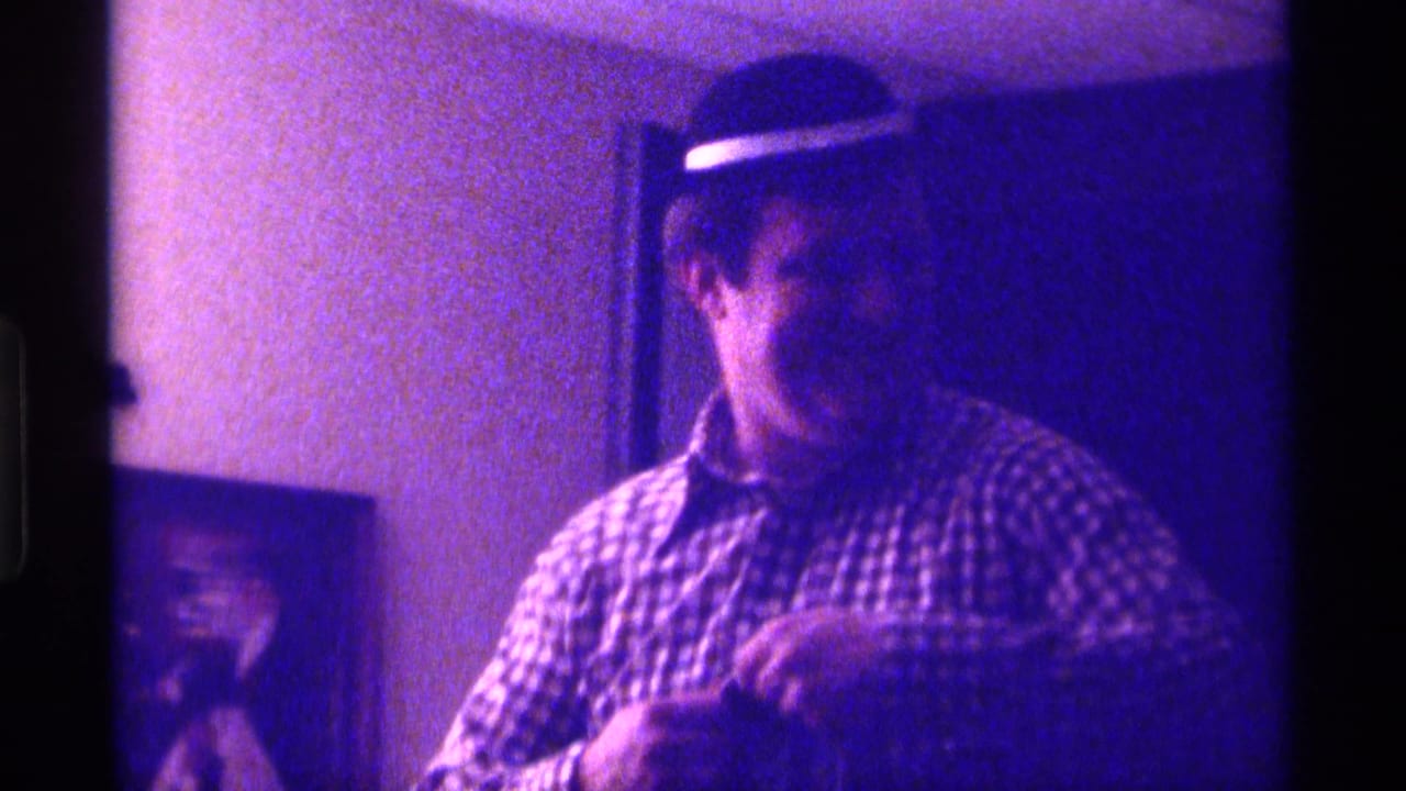 Man in a checkered shirt and hat faces forward while holding clothing.