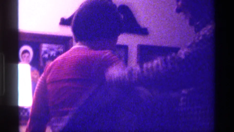 A child in a red top stands with back turned while the man in a checkered shirt adjusts a jacket in a private Kentucky interior.