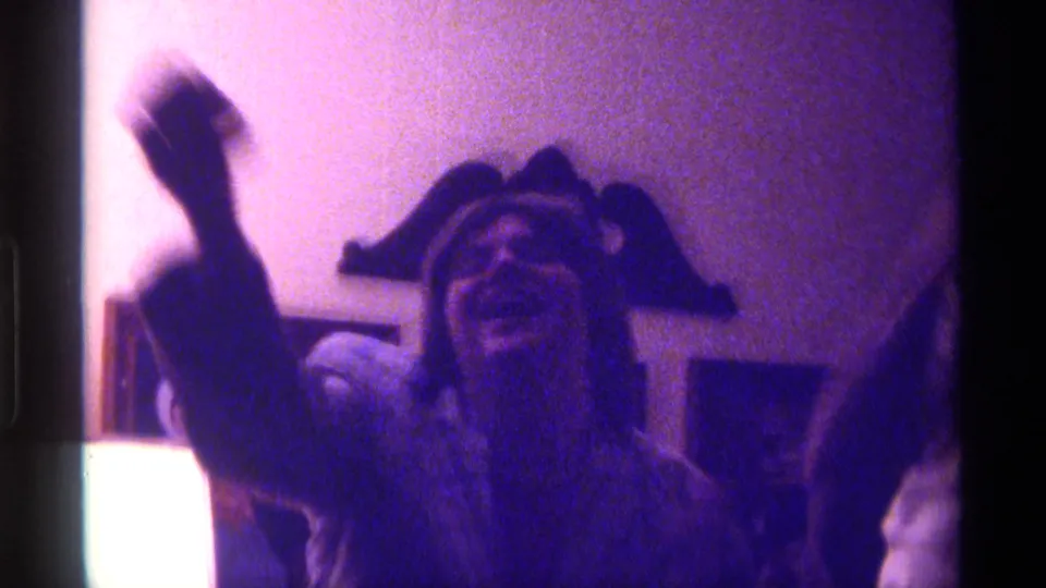 The woman lifts an arm and appears to laugh or react warmly, with the young man partly visible at the edge of the 8mm frame.