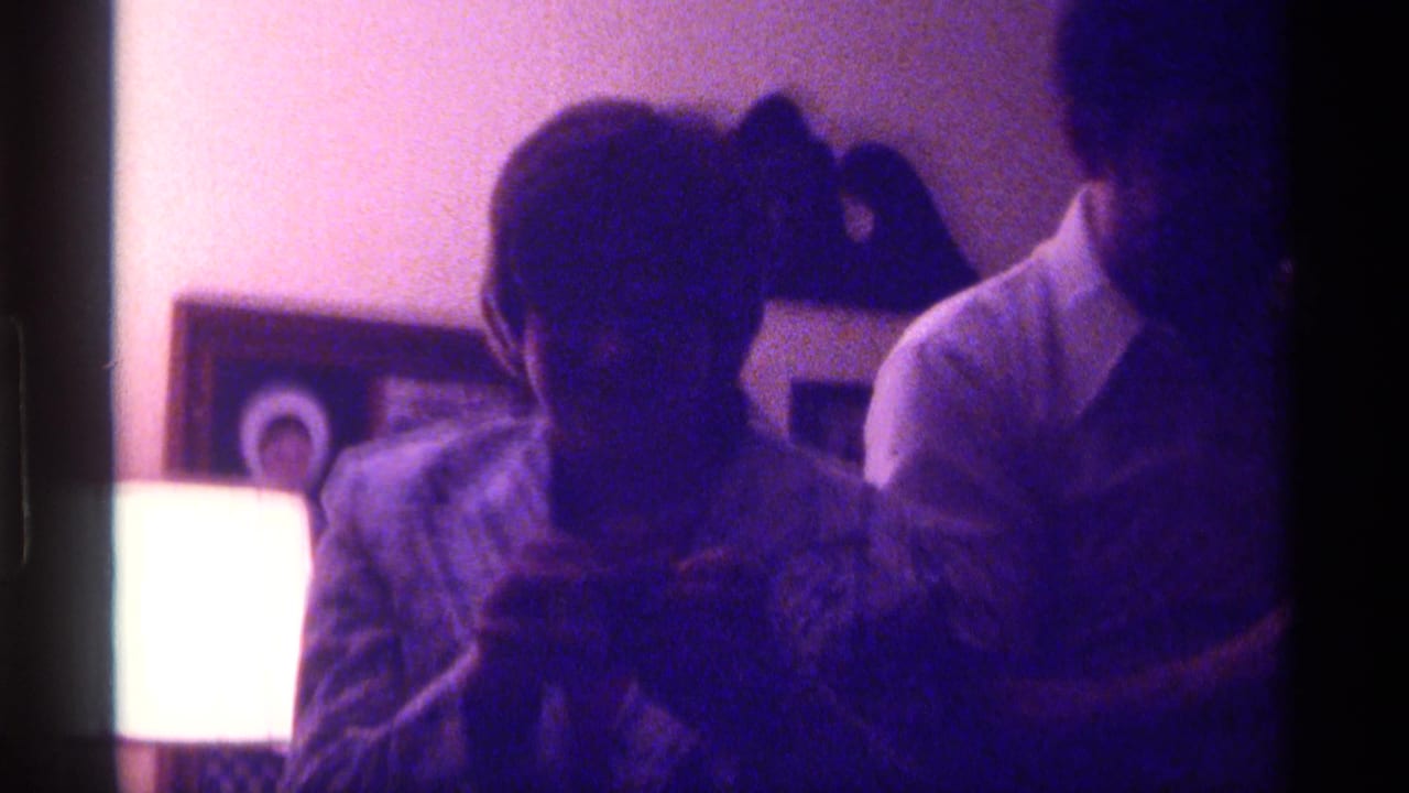 A seated person in silhouette with another person standing nearby in a dim room.