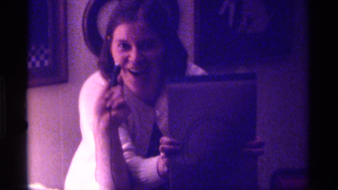 Smiling woman holds a notebook and raises a small object near her face.