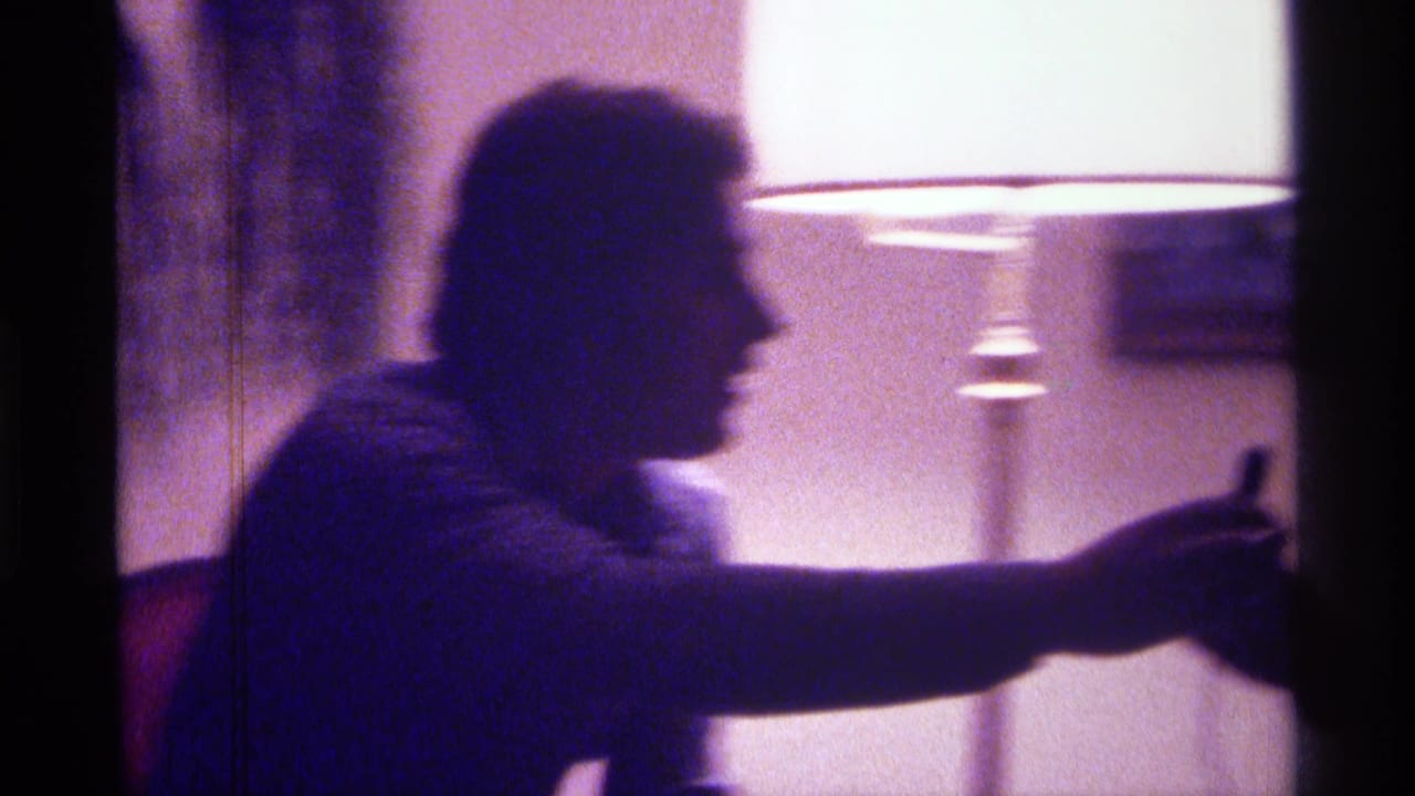 Man in profile reaches forward while seated near a bright floor lamp.