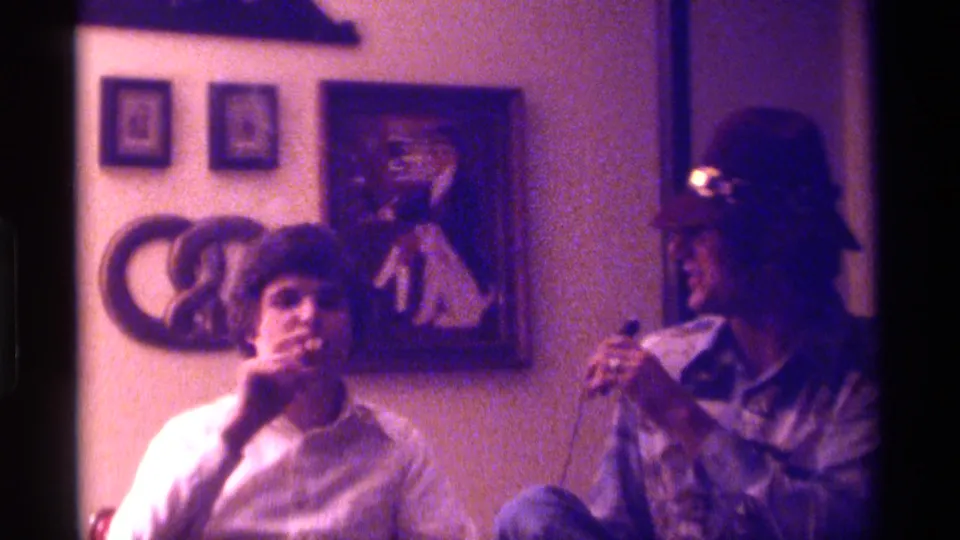 The 1976 Kentucky 8mm frame shows one man holding a cigar near his mouth while the man in a hat watches with the microphone nearby.