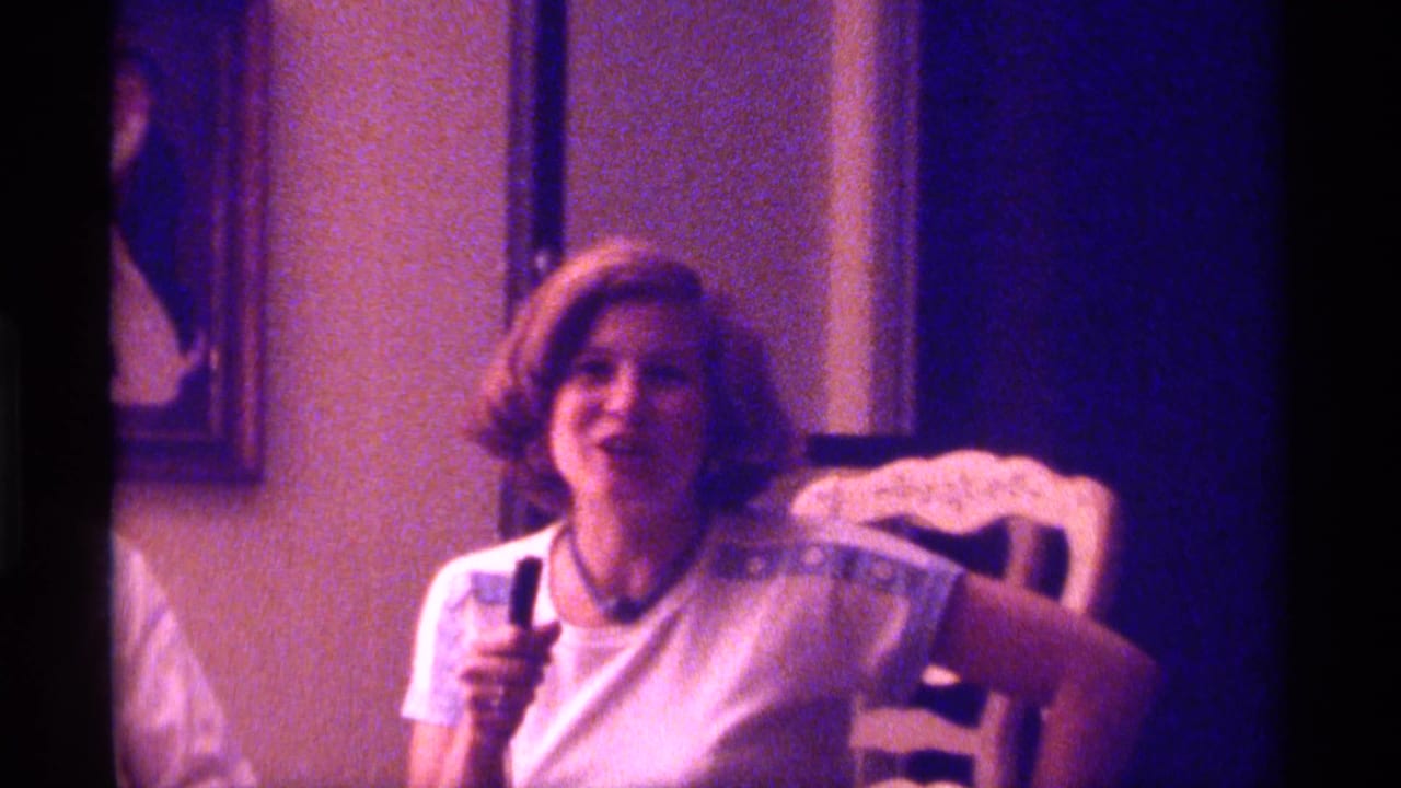 1976 Kentucky 8mm frame of a young woman with a short styled bob holding a wired microphone in a purple-blue lit interior.