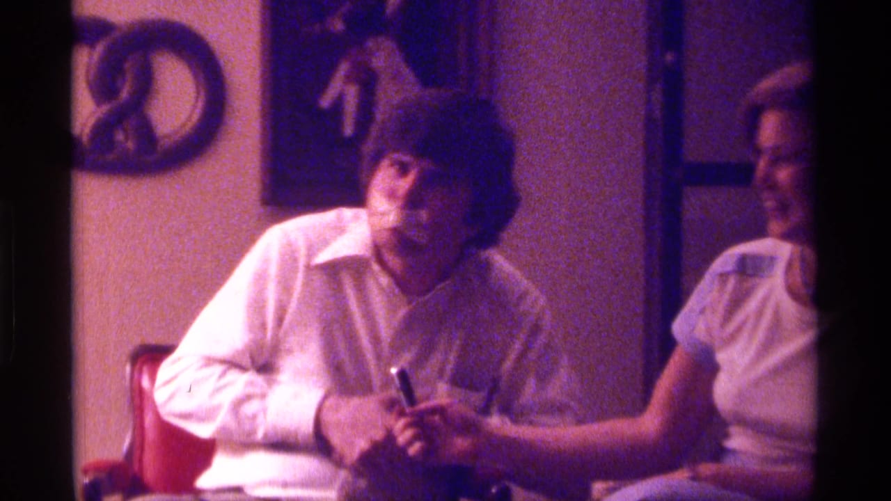Young man and woman sit close together at a table, both holding small objects in a dim room.