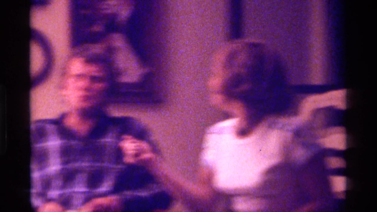 Two adults in a warmly lit room, one in plaid and one in a white T-shirt, with motion blur.