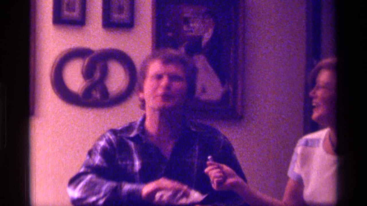 Man in a plaid shirt seated beside a woman in a white T-shirt in a decorated room.