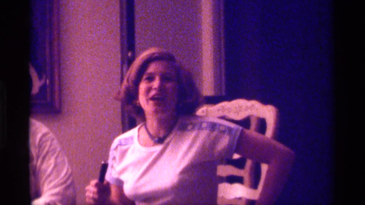 Woman in a white T-shirt sits at a dining chair, smiling during conversation.