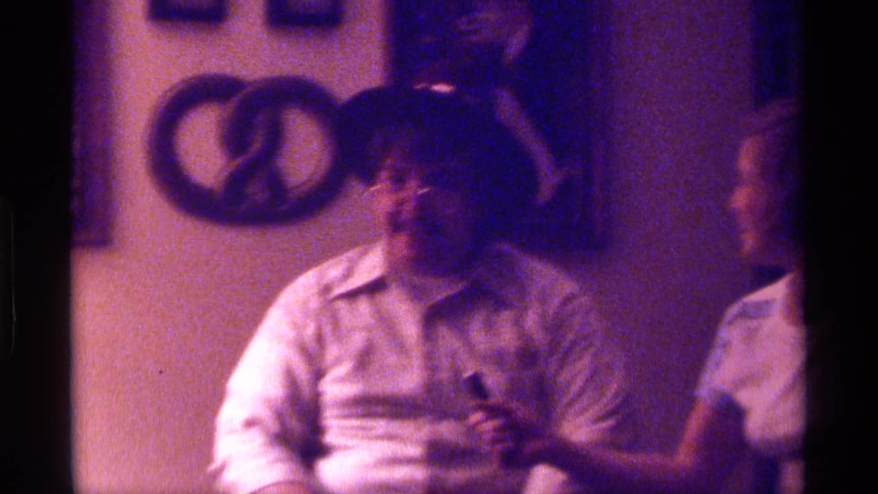 Man in a felt hat sits indoors with wall decor behind him.