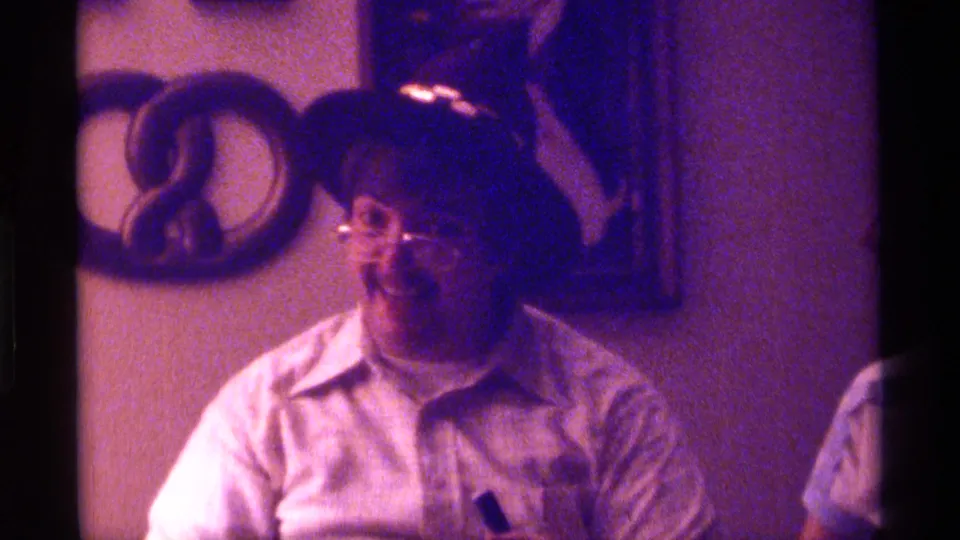The final frame shows the seated man in hat and glasses, with a partial person at the right edge and home interior decor behind him.