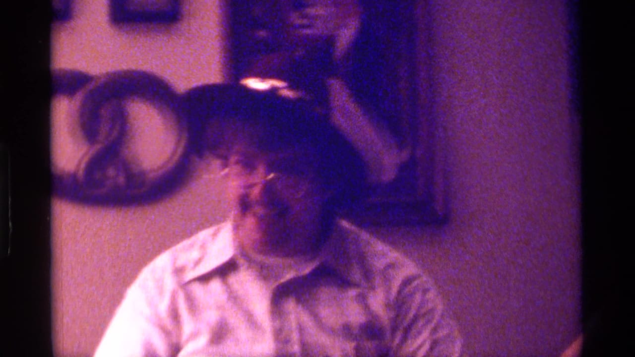 Man in glasses and a collared shirt laughs inside a warmly lit room.
