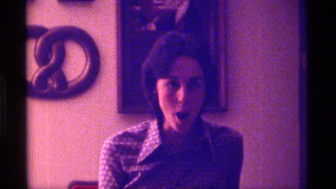 Young woman in a patterned blouse sits indoors beneath wall decorations.