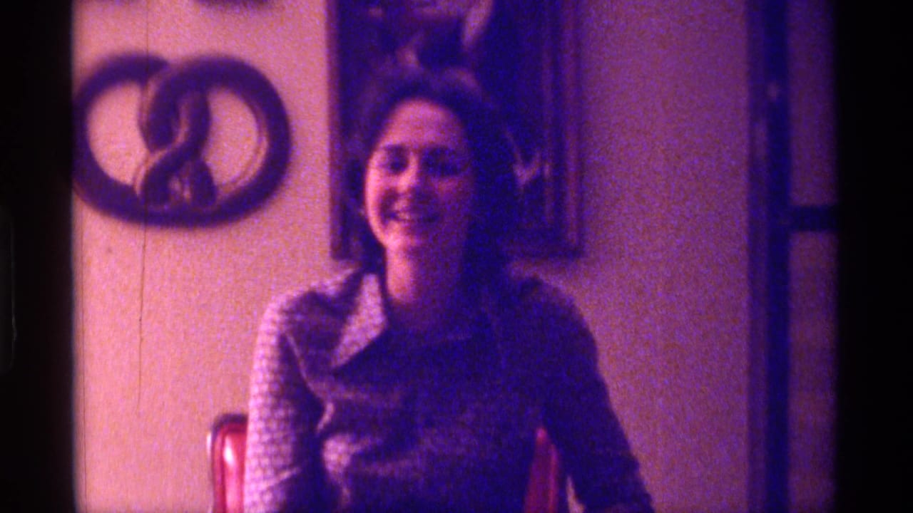Smiling woman seated indoors with wall decorations behind her.