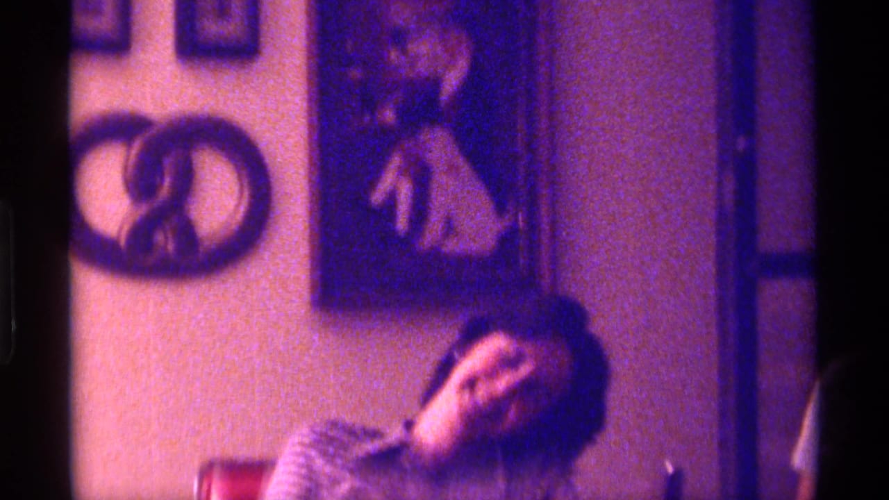 Woman laughs in a dim room with wall art and a pretzel-shaped decoration behind her.