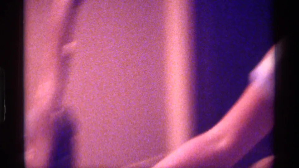 Soft, blurred 8mm frame shows a partially visible person and raised arm in the same dim interior setting.