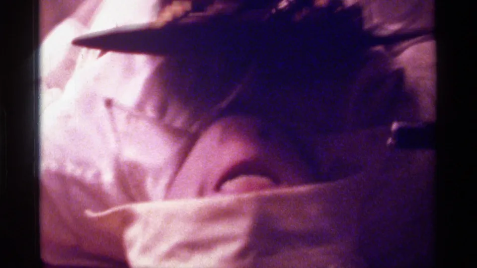 Close, soft-focus view of the reclining man with a dark hat over his eyes in a dim private interior.