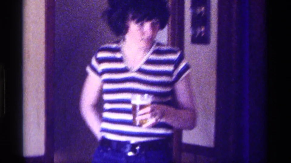 A woman in a striped sleeveless top appears in the private Kentucky home interior while holding a drink glass.