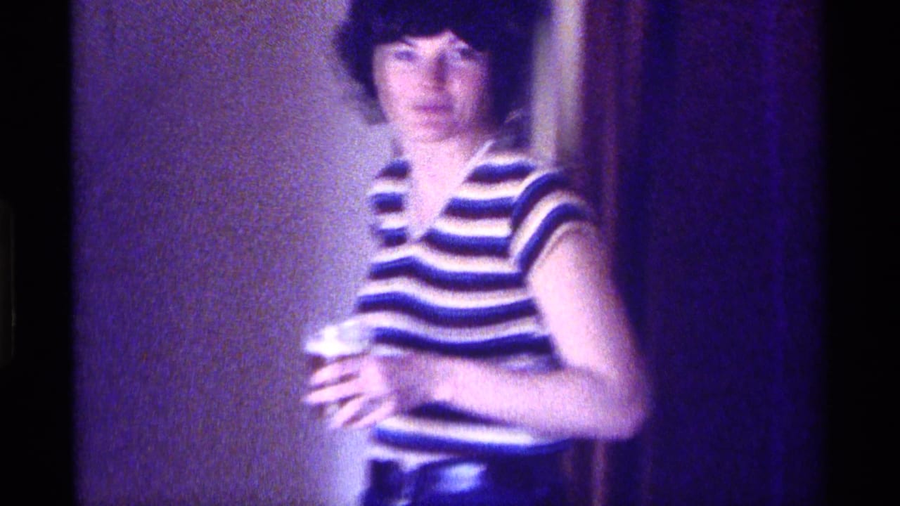 Woman in a striped top stands indoors holding a small cup.