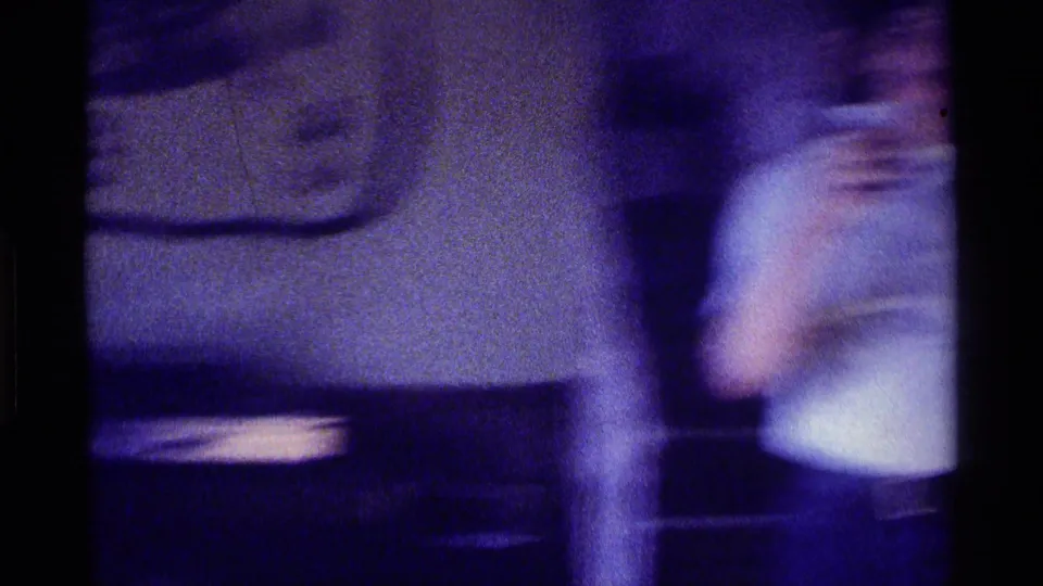 1976 Kentucky home-movie frame with motion-blurred figures crossing a private interior near upholstered furniture.