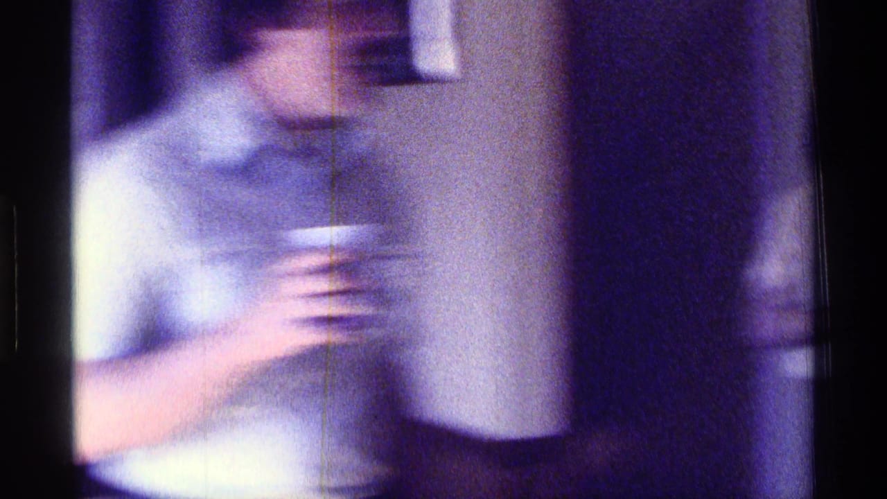 Motion-blurred 1976 Kentucky home-movie frame of a person passing through a private interior with a drink.