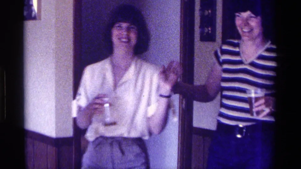 1976 Kentucky home-movie frame of two women laughing together indoors, one in a white blouse and one in a striped top.