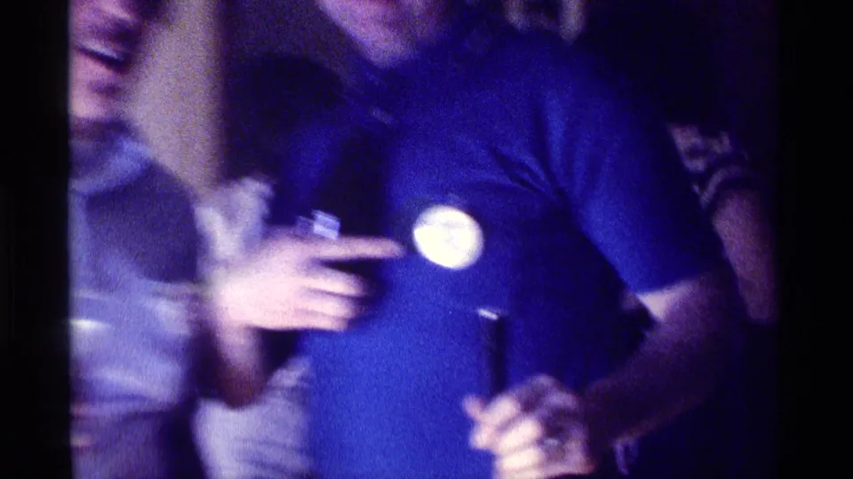 1976 Kentucky party frame showing a man in a blue polo with a round button as another adult leans into the shot nearby.