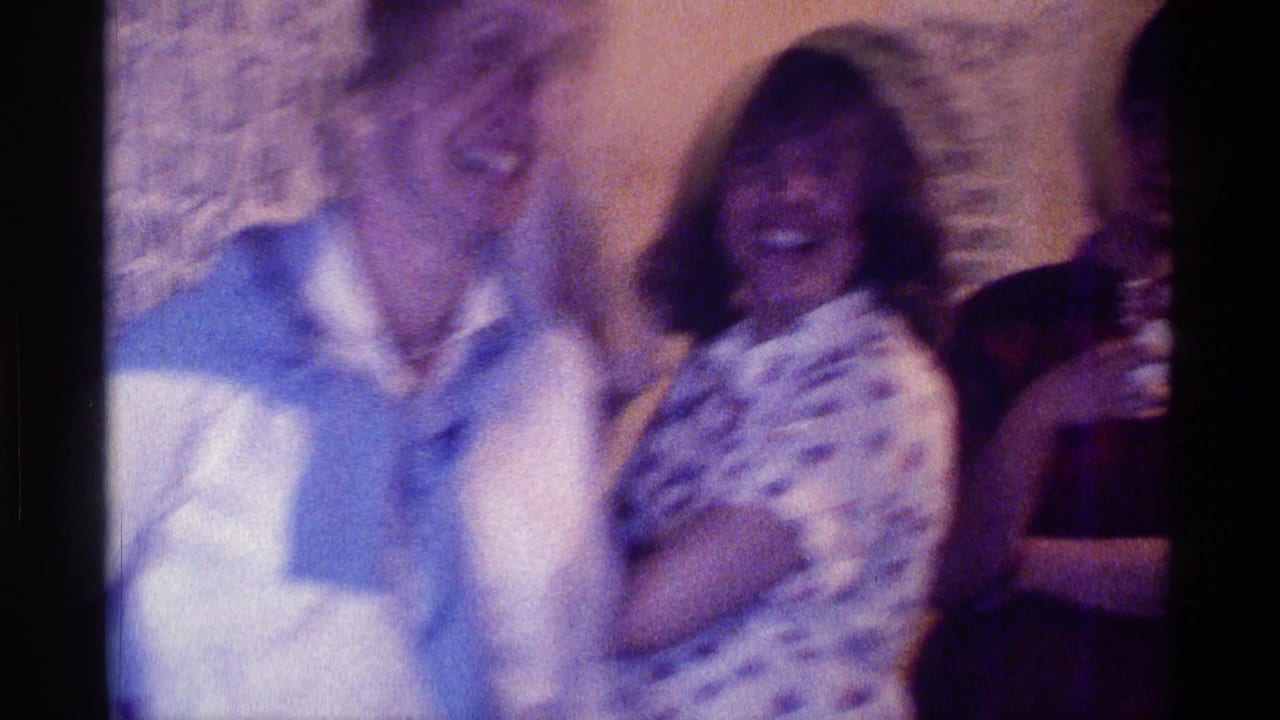 Several adults laughing together indoors, with one person holding a drink at the edge.