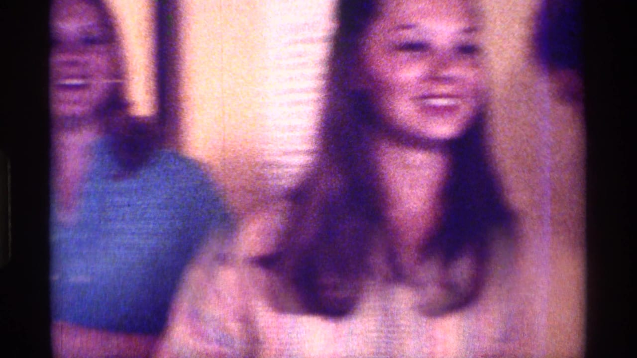 Two women smiling indoors, with one centered near a window blind.