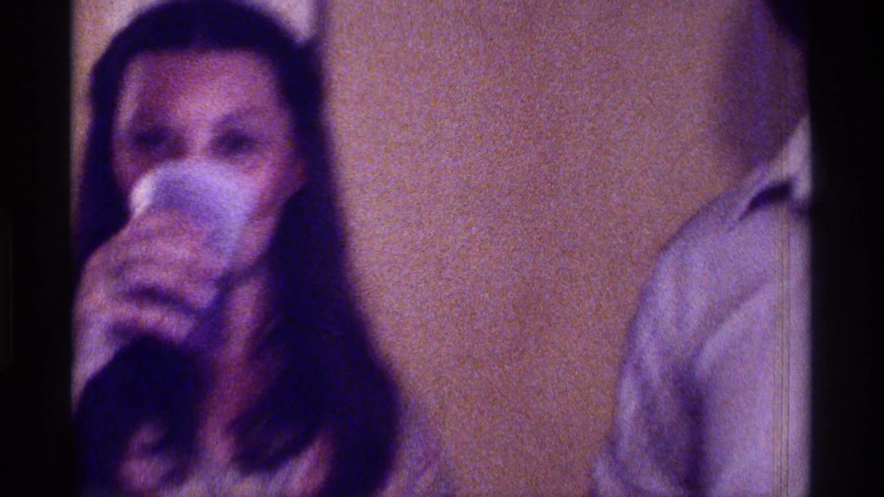 Woman drinking from a cup beside another adult in a dim indoor room.