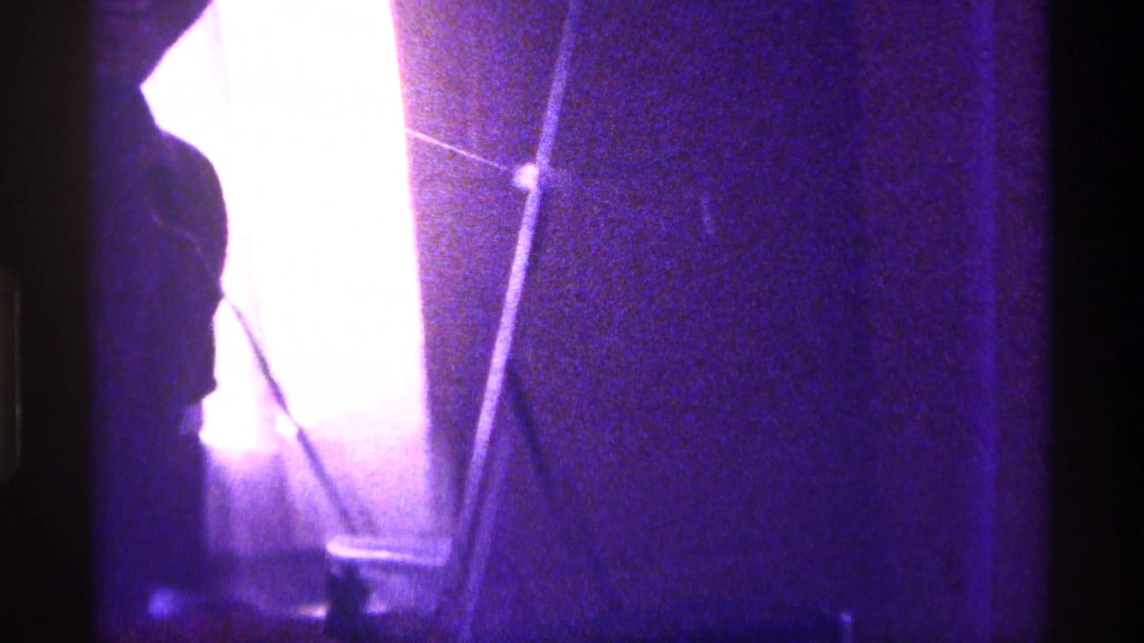 Dim purple-tinted interior with a silhouetted person near a bright window and tripod.