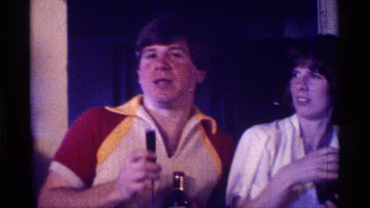 Man speaks into a microphone while a woman stands beside him at a party.