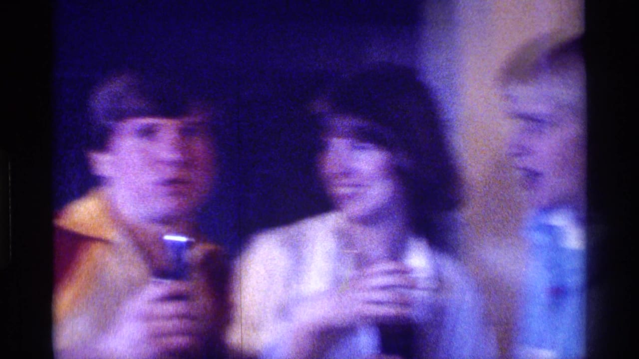 Young man with a microphone sits beside a smiling woman at a dim party.