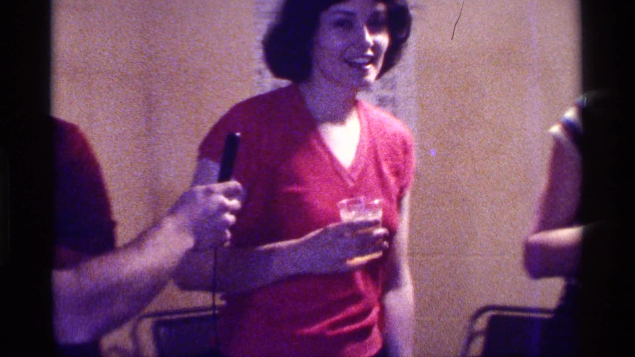 A woman in a red top smiles while a handheld microphone is held toward her.