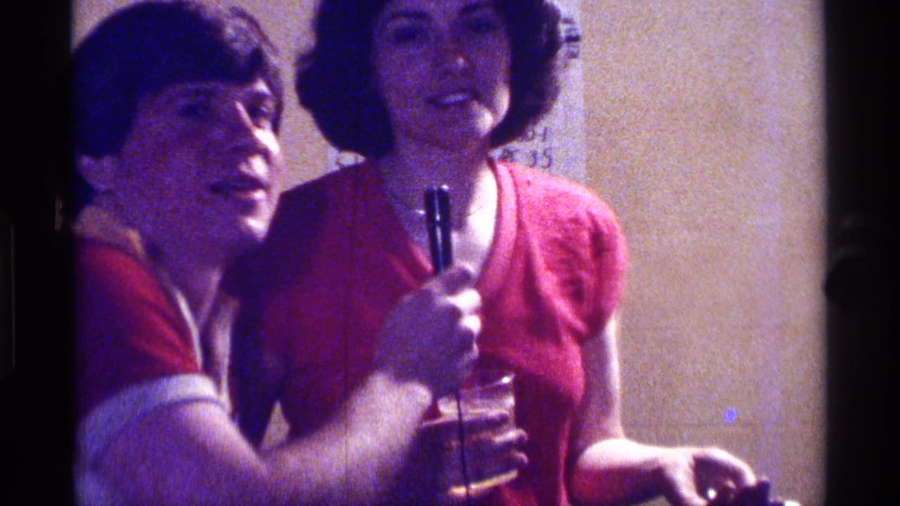 Man in a red shirt holds a microphone toward a woman in a red top indoors.