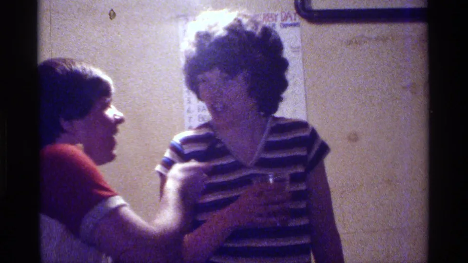 The man holds the microphone toward the woman in a striped shirt while a partially visible wall poster appears behind them indoors.