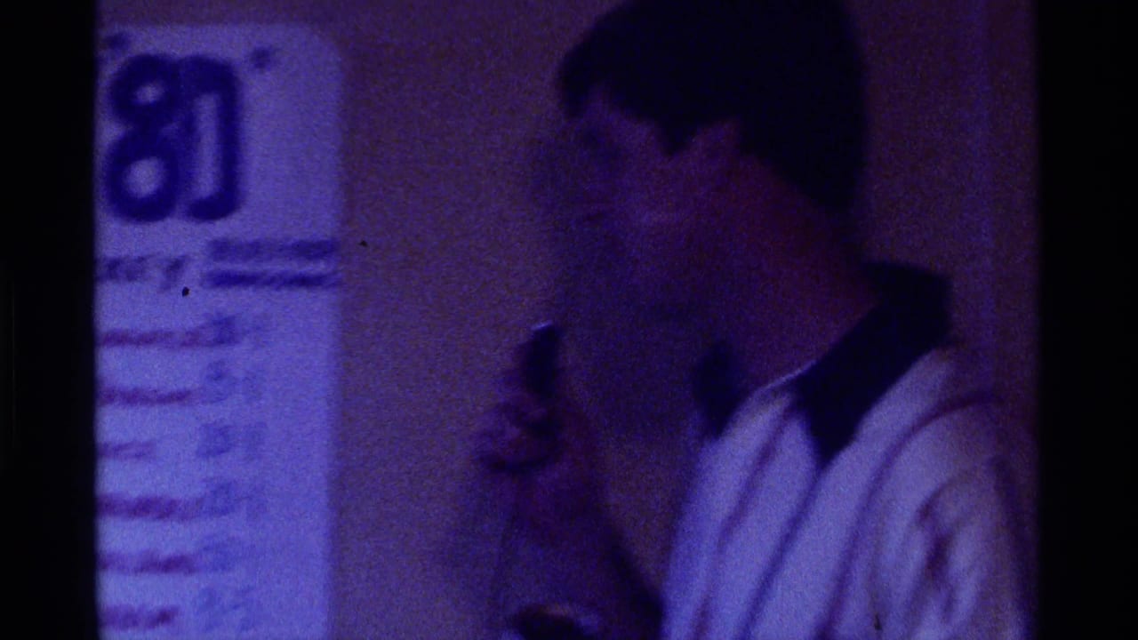 Man in a white shirt holds a microphone beside a Kentucky 80 sign indoors.