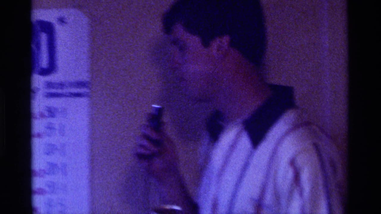 Man in a white shirt turns sideways while holding a microphone near a sign.