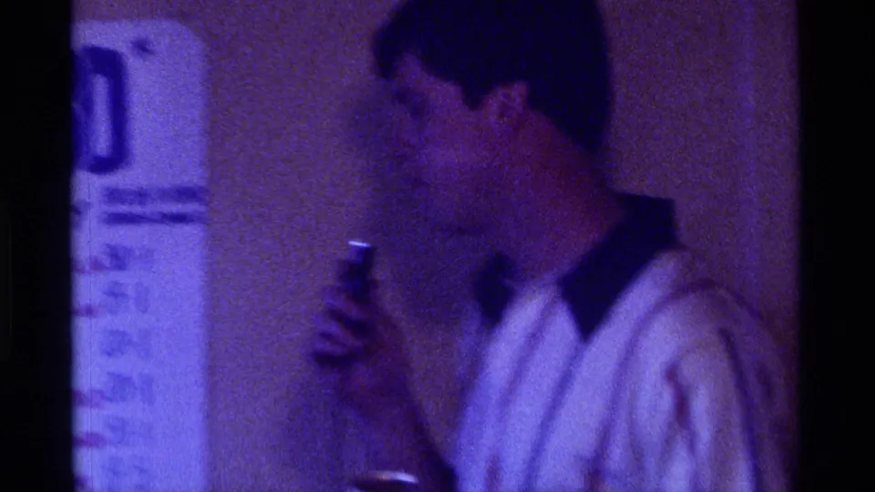 1976 Kentucky 8mm frame showing a man in profile with a handheld microphone beside a partially visible Kentucky 80 sign.