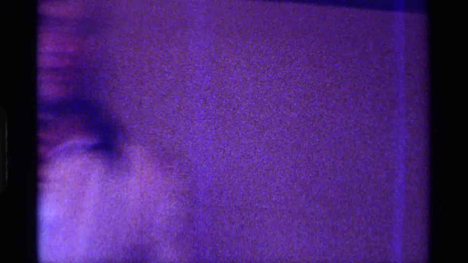 Soft, blurred 8mm frame from the indoor Kentucky clip, with a partial figure or wall surface under purple low light.
