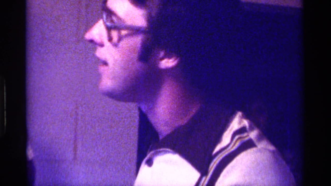 Man in glasses shown in profile under purple-tinted indoor light.