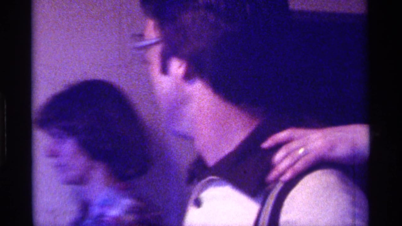 Man turns toward a woman moving behind him in an indoor room.